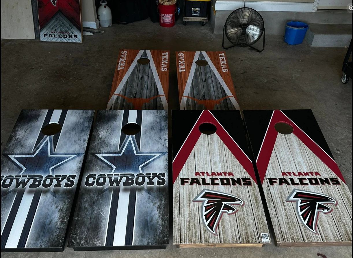 Finished Cowboys, Atlanta Falcons and Texas Longhorns cornhole sets on a garage floor